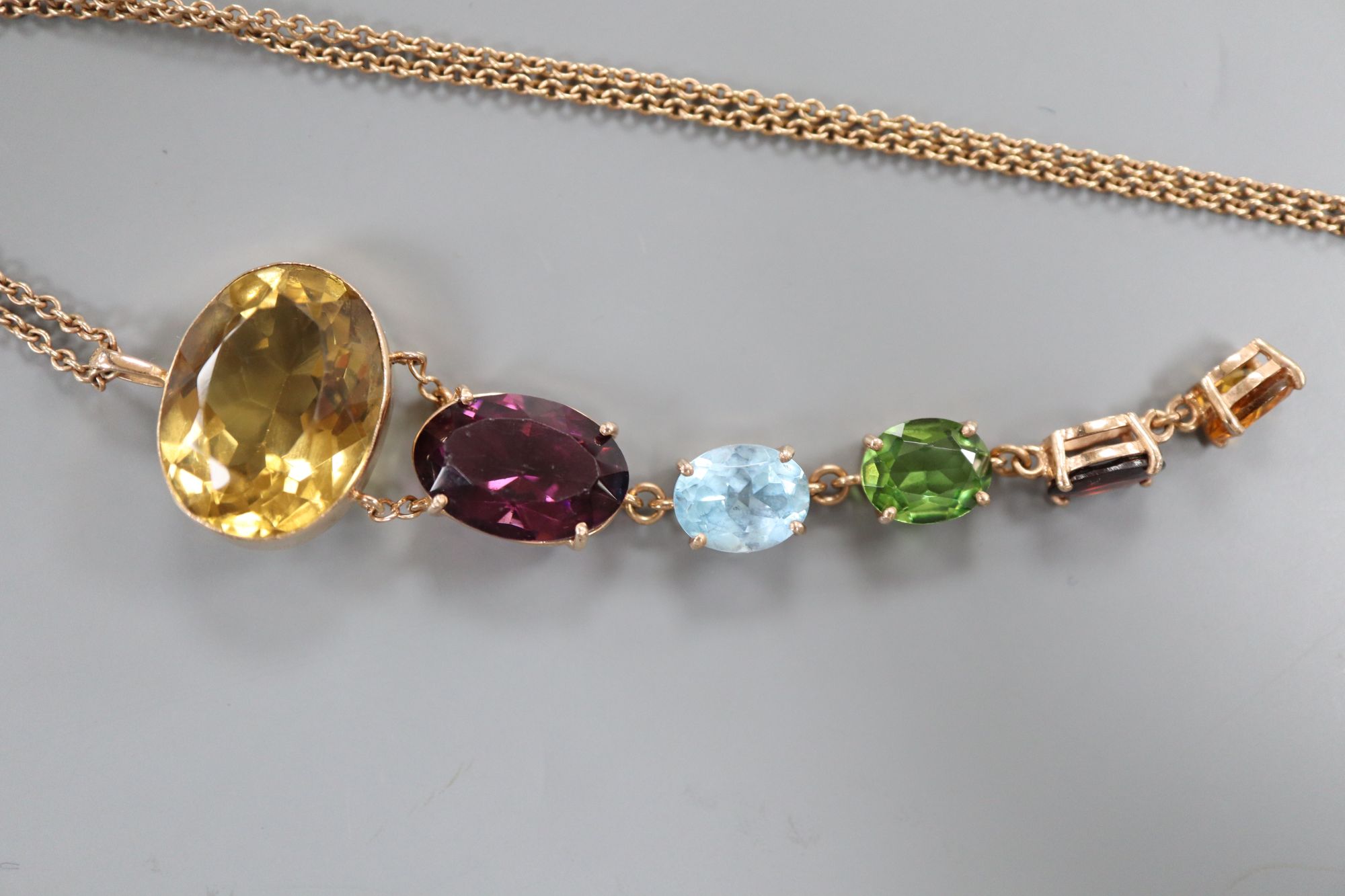 A yellow metal and graduated oval multi gem set pendant, on a yellow metal chain,